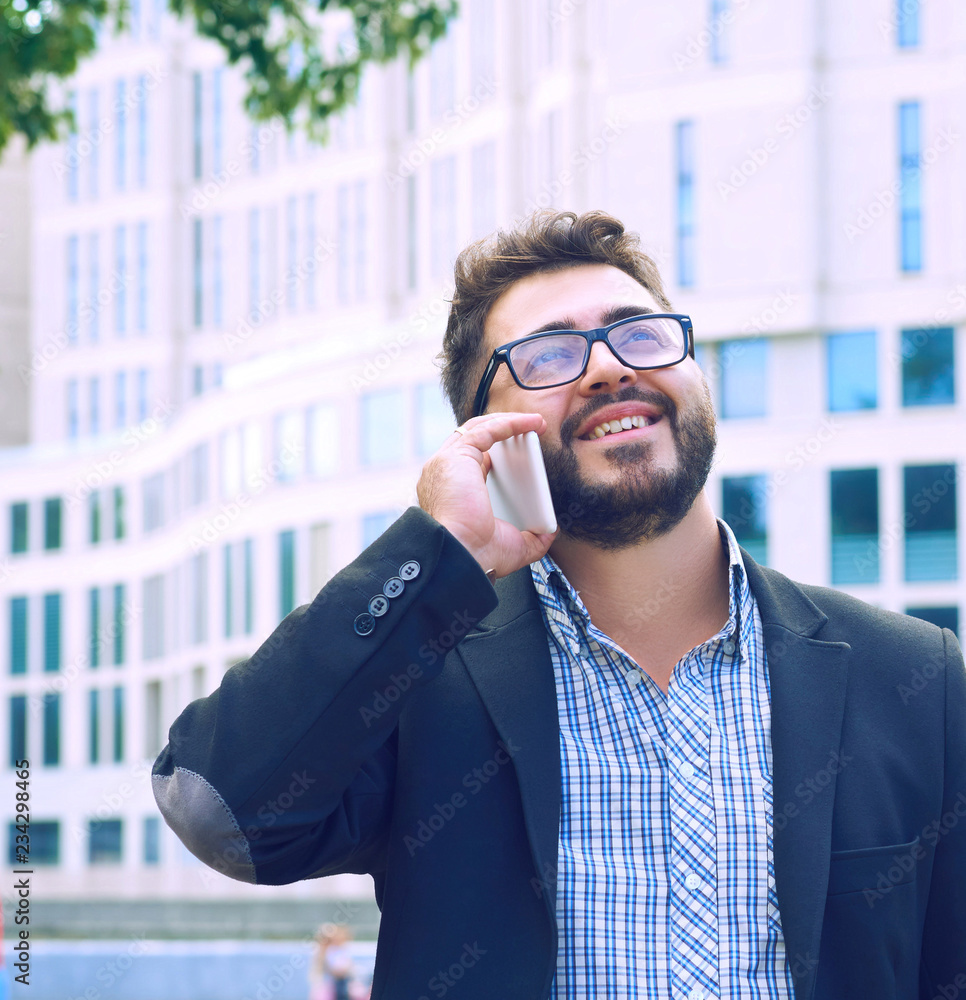Young businessman in glasses with a beard talking on the phone walking down the street. Young businessman in glasses with a beard talking on the phone walking down the street.