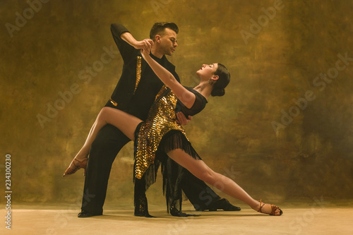 Obraz na plátně The young dance ballroom couple in gold dress dancing in sensual pose on studio background