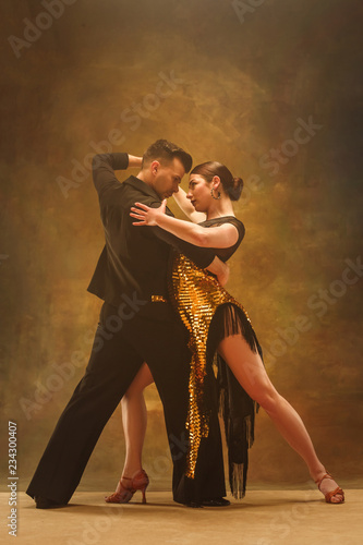 The young dance ballroom couple in gold dress dancing in sensual pose on studio background. Professional dancers dancing tango. Ballroom dance concept. Human emotions - love and passion