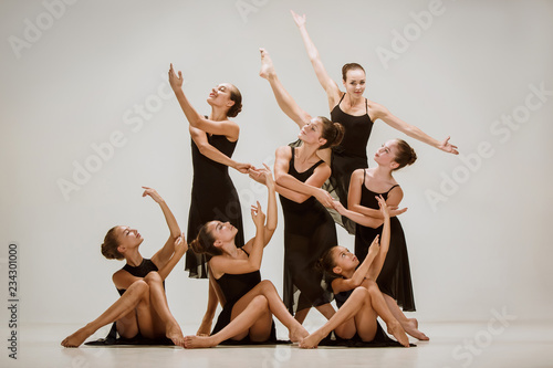 The group of modern ballet dancers dancing on gray studio background