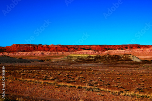 Field with colorful mountains under bright blue sky.
