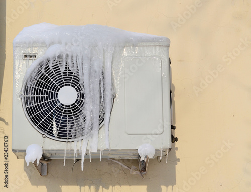 The conditioner covered with icicles on a yellow wall