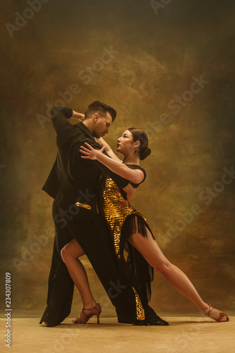 Obraz na plátně The young dance ballroom couple in gold dress dancing in sensual pose on studio background