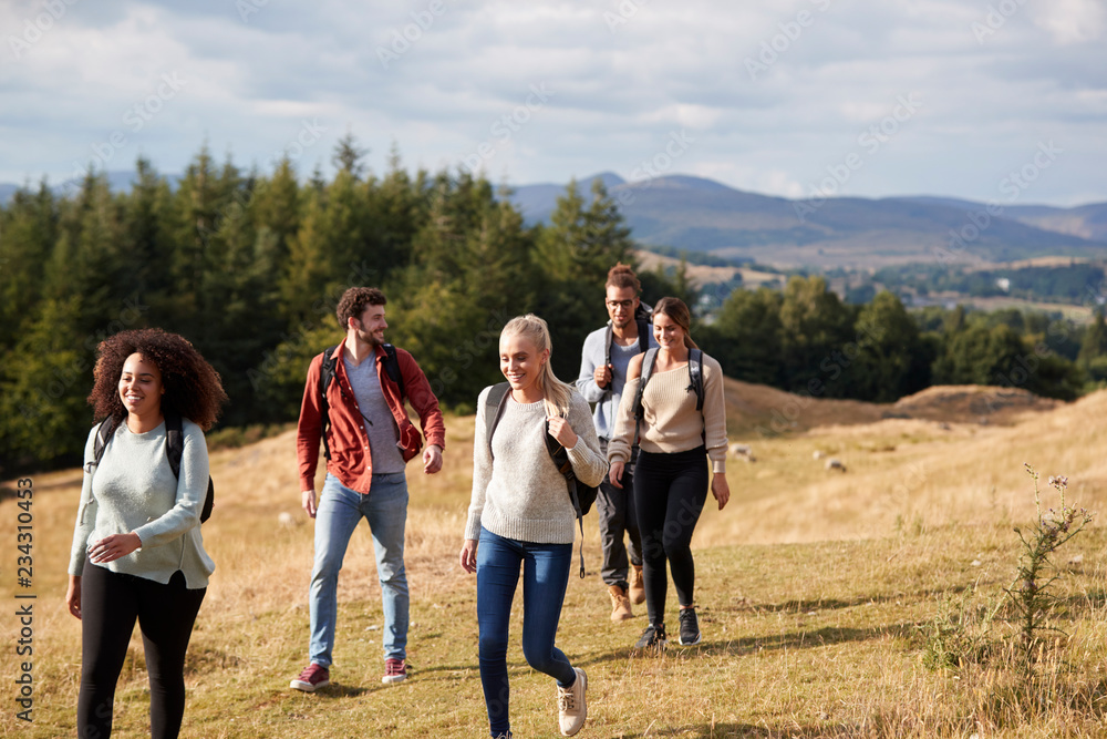 Multi ethnic group of five happy young adult friends talking as they walk on a rural path during a mountain hike Multi ethnic group of five happy young adult friends talking as they walk on a rural path during a mountain hike