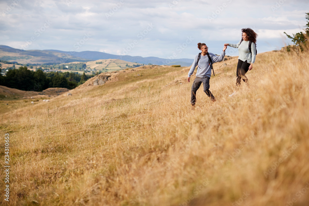 Mixed race young adult couple holding hands while walking walking down a hill during a mountain hike Mixed race young adult couple holding hands while walking walking down a hill during a mountain hike