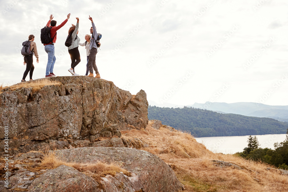A group of five happy young adult friends cheer with their arms in the air at the summit during mountain hike A group of five happy young adult friends cheer with their arms in the air at the summit during mountain hike