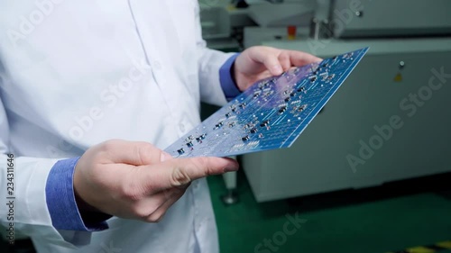 The engineer in a white robe inspect ready motherboard. PCB Processing on CNC machine, Production of electronic components at high-tech factory. Close up