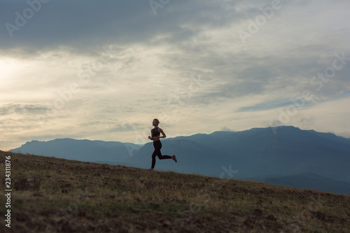 Schilderij op canvas Slim girl wearing black sport outfit is jogging in mountains uphill, beautiful l