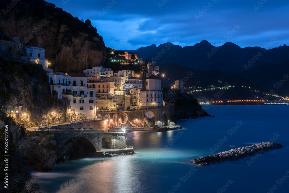 Amalfi coast with street lights in the morning twilight and reflection on the sea and  storm surge barrier breakwater. Italy.  Long exposure.