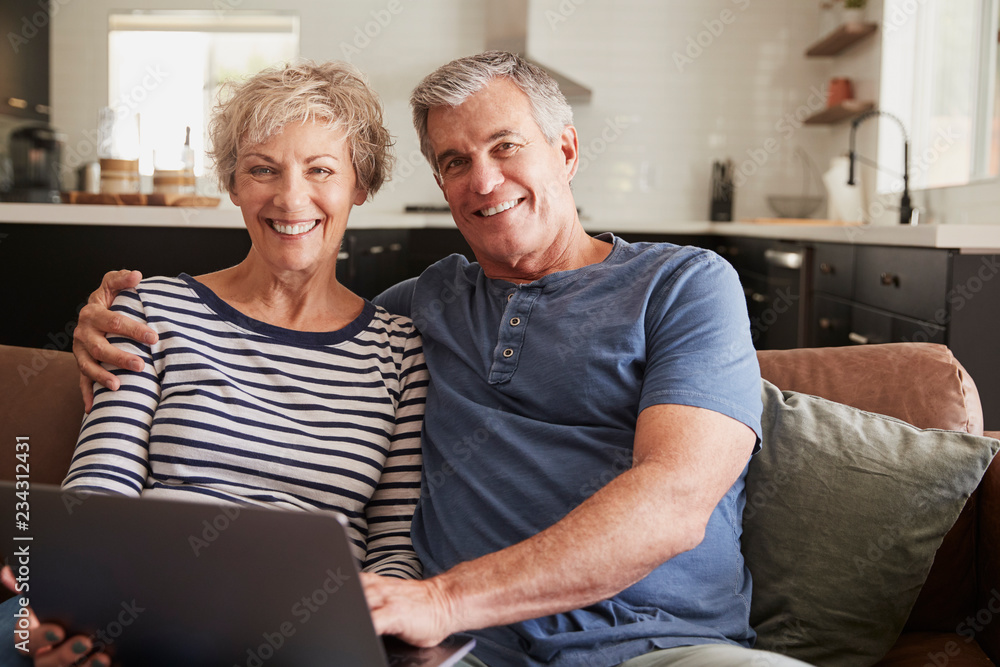 Senior couple sitting on couch use laptop, smiling to camera Senior couple sitting on couch use laptop, smiling to camera