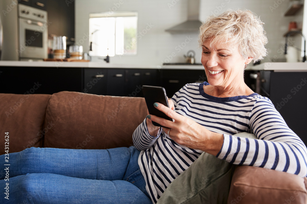 Senior white woman sitting on couch at home using smartphone Senior white woman sitting on couch at home using smartphone