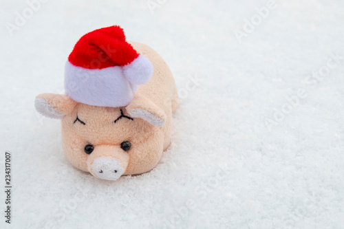 Toy pink pig red Santa Claus hat on white snow. The concept of the New Year and Christmas. Copy space.