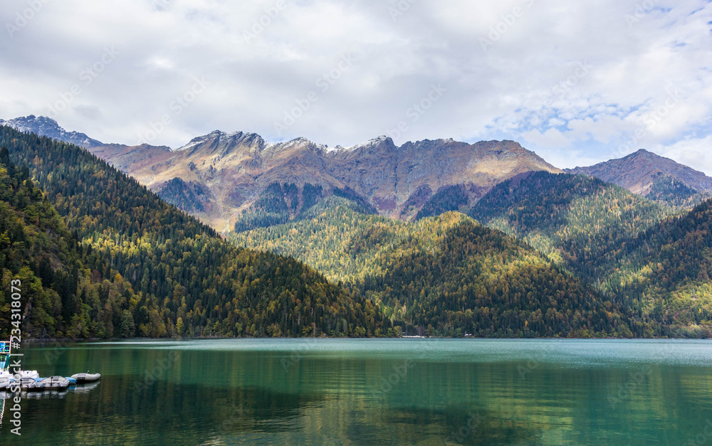 Caucasus. Abkhazia. Riza lake, autumn forest and white snow peaks, reflecting in the calm water of the lake.