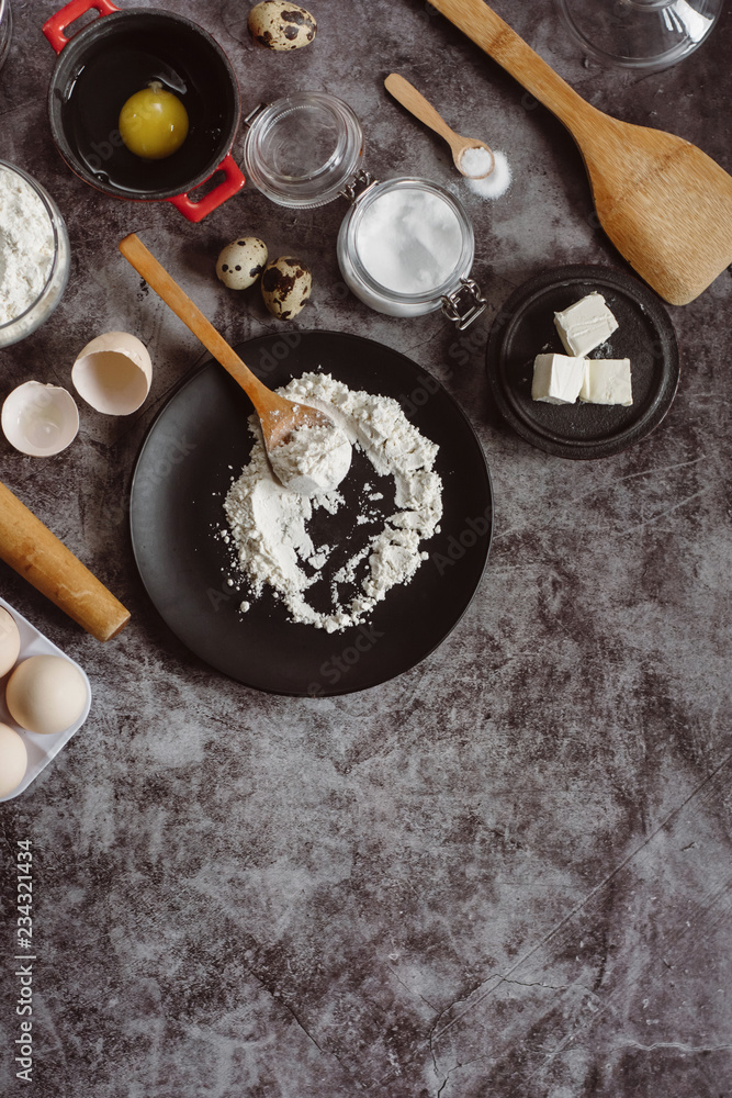 Ingredients and utensils for baking. Spoon with flour, dishes, eggs, butter salt and rolling pin on a grey background. Flat lay. Text space Ingredients and utensils for baking. Spoon with flour, dishes, eggs, butter salt and rolling pin on a grey background. Flat lay. Text space