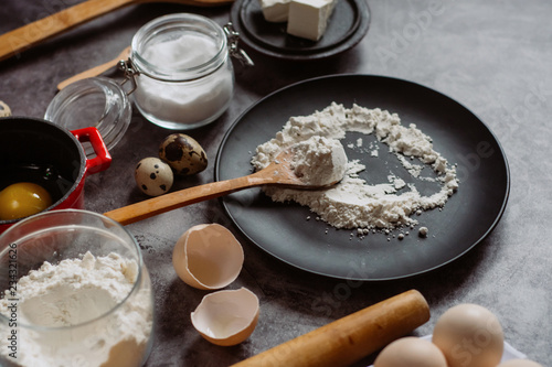 Ingredients and utensils for baking. Spoon with flour, dishes, eggs, butter salt and rolling pin on a grey background. Flat lay. 