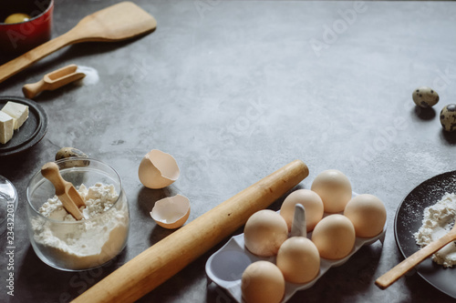 Ingredients and utensils for baking. Spoon with flour, dishes, eggs, butter salt and rolling pin on a grey background. Flat lay. Text space