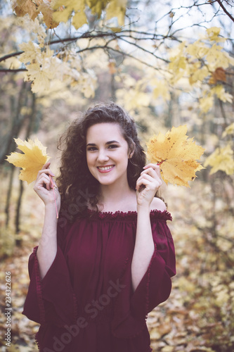 Happy girl in an atumn park holding maple leaves