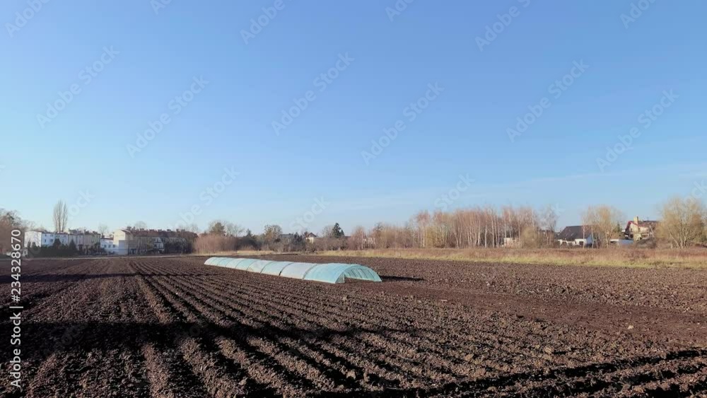 Empty plowed field with dark soil at beginning of spring or end of autumn. Plowing field soil after autumn works. Greenhouse in countryside - black soil fields in autumn season. Empty plowed field with dark soil at beginning of spring or end of autumn. Plowing field soil after autumn works. Greenhouse in countryside - black soil fields in autumn season.