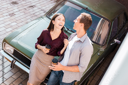 Couple of traveler sitting on hatchback of car and looking to each other near the road during holiday.Young couple tourist enjoying on vacation, eurotour trip together on their honeymoon photo