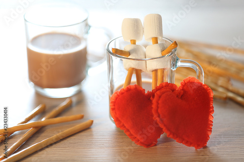 Two cups of chocolate, two hearts and sweet sticks on a table with a blurred background.