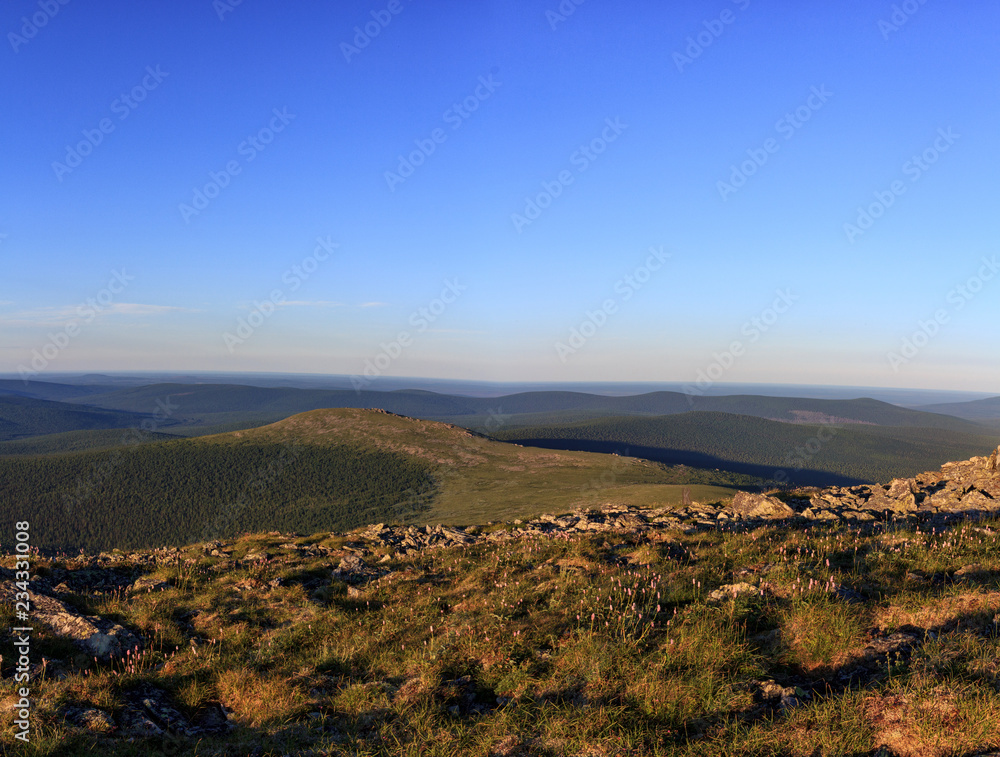 Mountain valley of the Northern Urals in summer. Traveling in the Northern Urals. Beautiful panorama of mountain valleys and passes and a blue sky.