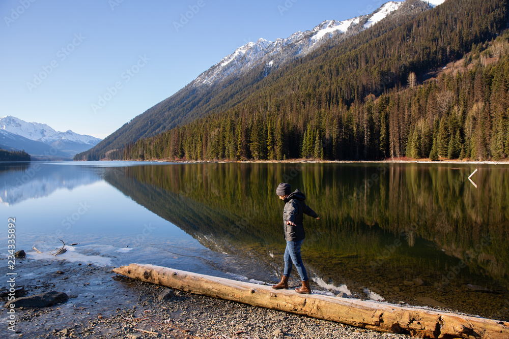 British Columbia Canada, Duffy Lake with smooth water reflection and mountains in backgrounds and woman walking balancing on log