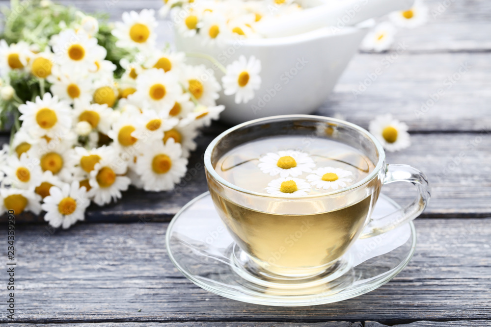 Cup of tea with chamomile flowers on grey wooden table