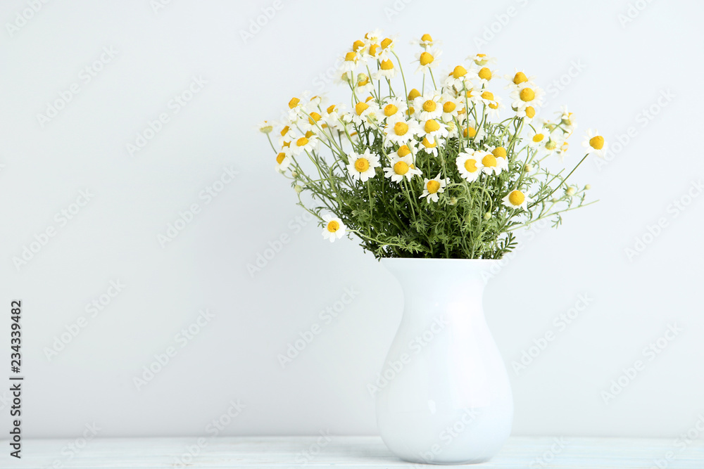 Bouquet of chamomile flowers in vase on grey background