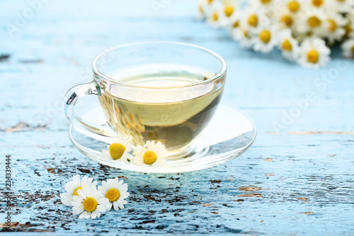 Cup of tea with chamomile flowers on blue wooden table