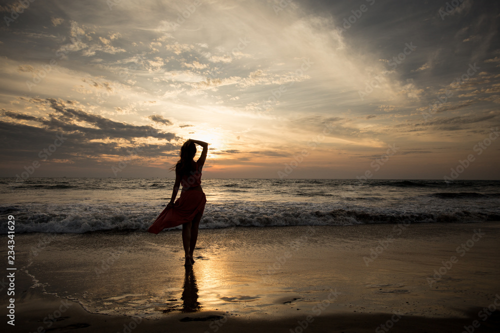 Silhouette of a young woman at an incredible sunset in cloudy weather by the sea. The concept of freedom. Rest on the sea. Enjoying life. Waves are coming.