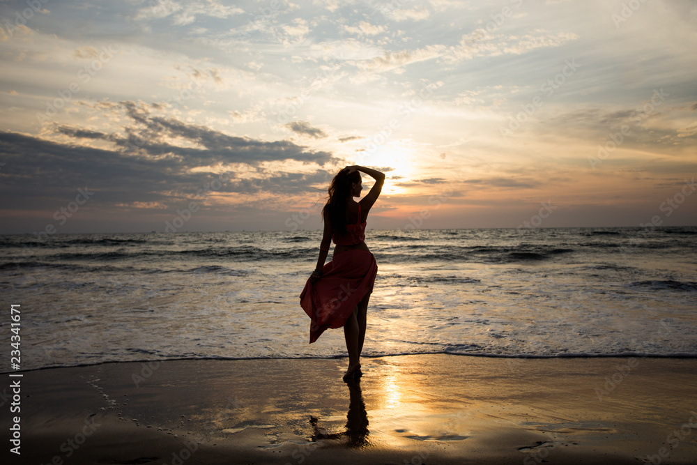 Silhouette of a young woman at an incredible sunset in cloudy weather by the sea. The concept of freedom. Rest on the sea. Enjoying life. Waves are coming.
