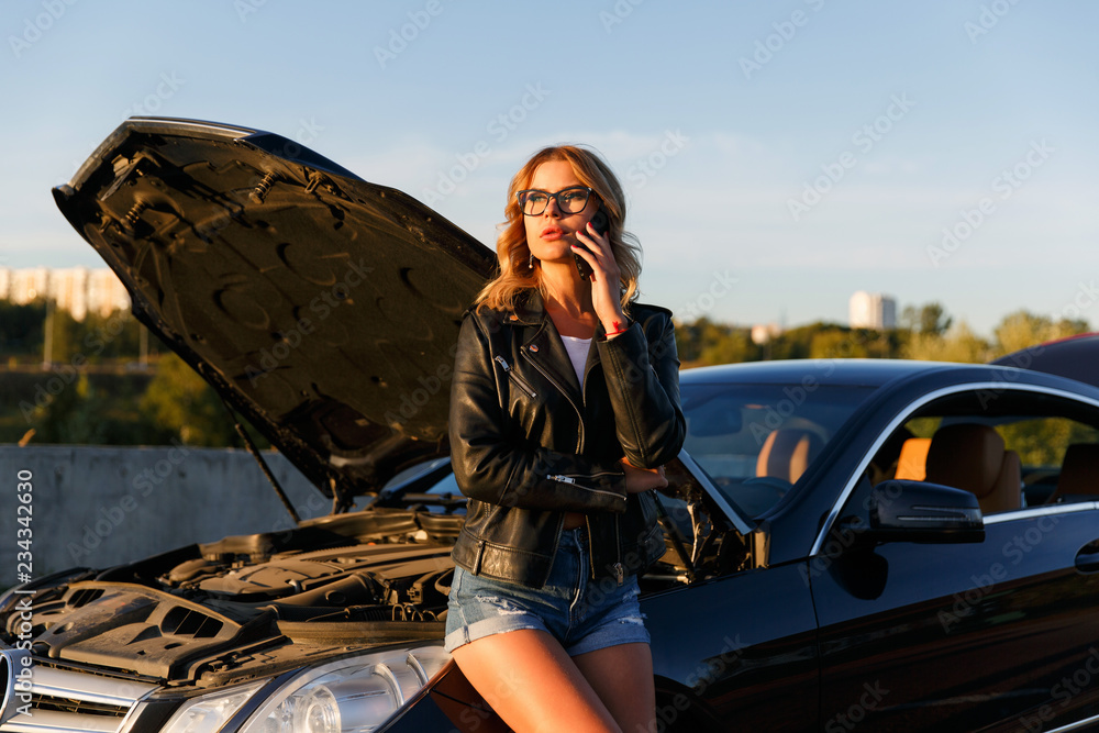 Φωτογραφία Photo of young woman talking on phone near broken car with open hood