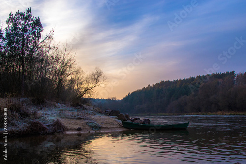 landscape by the river: a wooden boat at the shore and the first frost