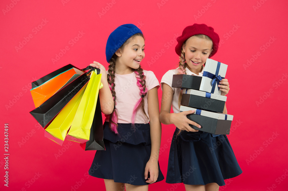 Shopaholic concept. Shopping become fun with best friends. Kids cute schoolgirls hold bunch shopping bags. Children satisfied by shopping red background. Obsessed with shopping and clothing malls