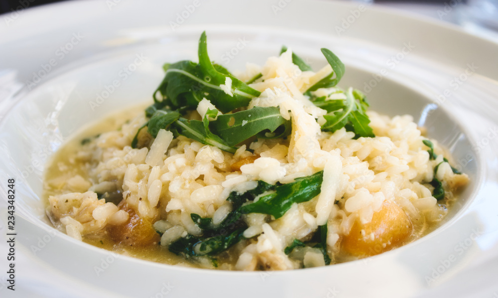 Pumpkin risotto with rocket leaves and parmesan cheese shavings in a white dish 