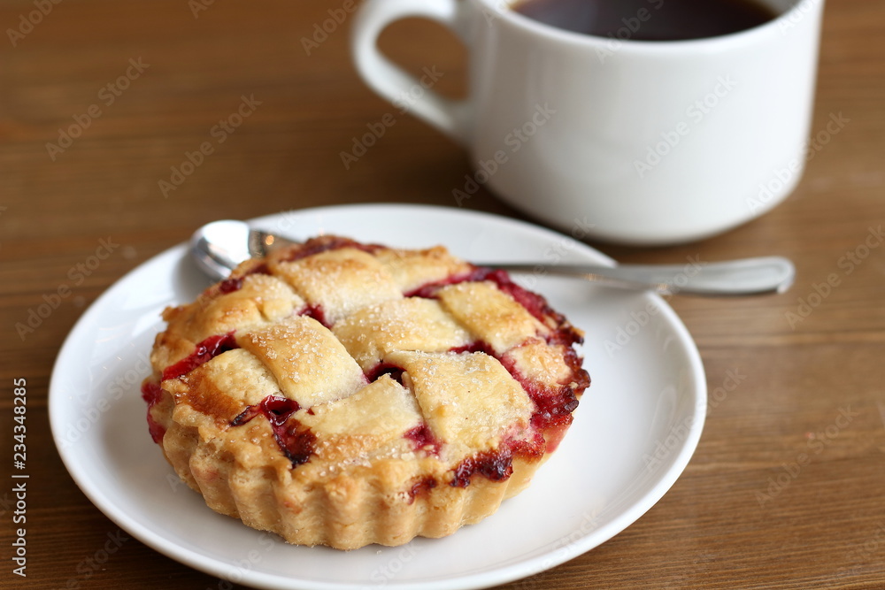 Home made cherry pie with lattice and metal spoon on the white plate and cup of coffee americano on the wooden table Home made cherry pie with lattice and metal spoon on the white plate and cup of coffee americano on the wooden table