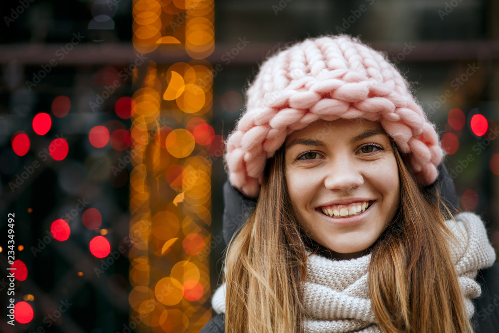 Happy blonde girl wearing warm winter outfit celebrating Christmas at the garlands blurred background. Space for text Happy blonde girl wearing warm winter outfit celebrating Christmas at the garlands blurred background. Space for text