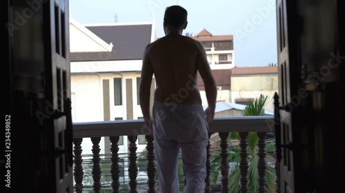 Man in pyjama bottom going on his terrace and admires the view  photo