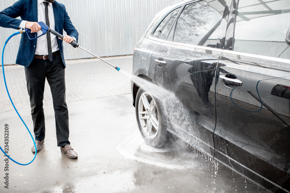 Businessman dressed in the suit washing his luxury car with washing gun