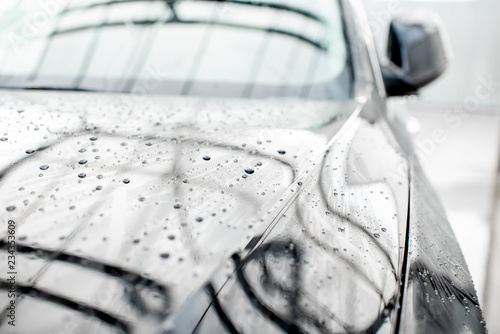 Close-up of a luxury black car during the washing process with water dropes outdoors