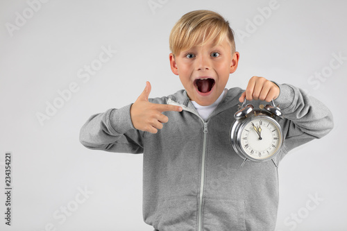 little blond boy has an alarm clock and is surprised, shows its high time with open mouth. 