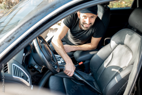 Professional cleaner in black t-shirt and cap vacuuming leather seats of a luxury car