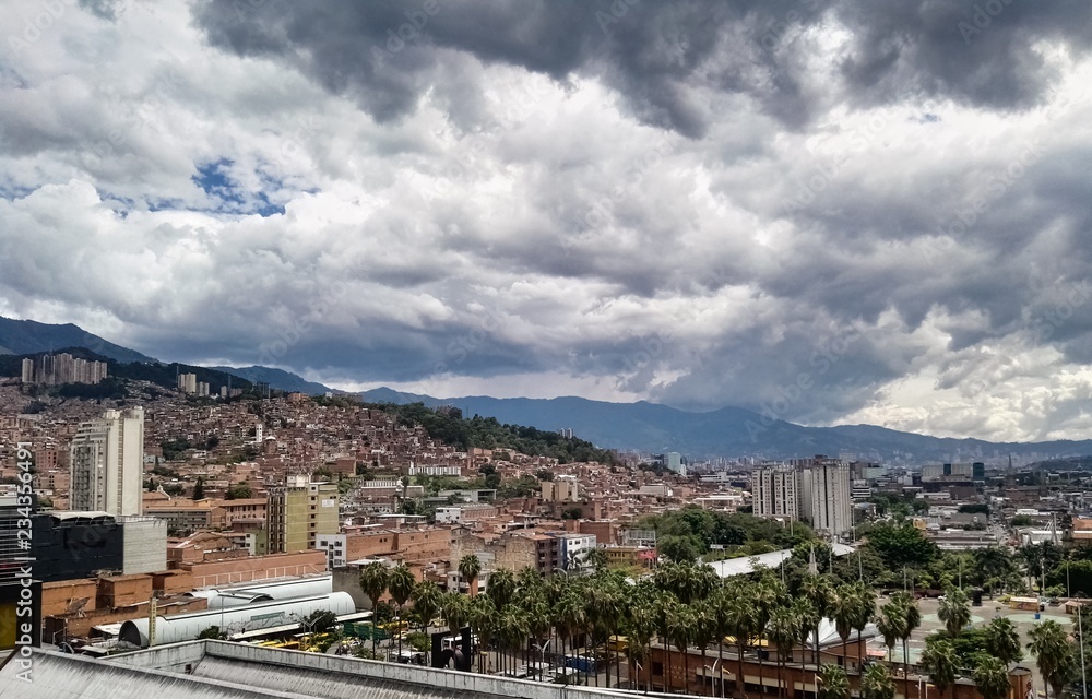 Panoramic view of Medellin in the Aburra Valley (Antioquia, Colombia). Dramatic storm sky, many palm trees and brick buildings.