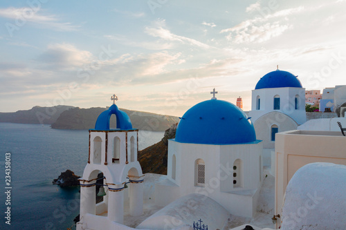 traditional white greek village Oia of Santorini, with blue domes of churches in sunset light, Greece