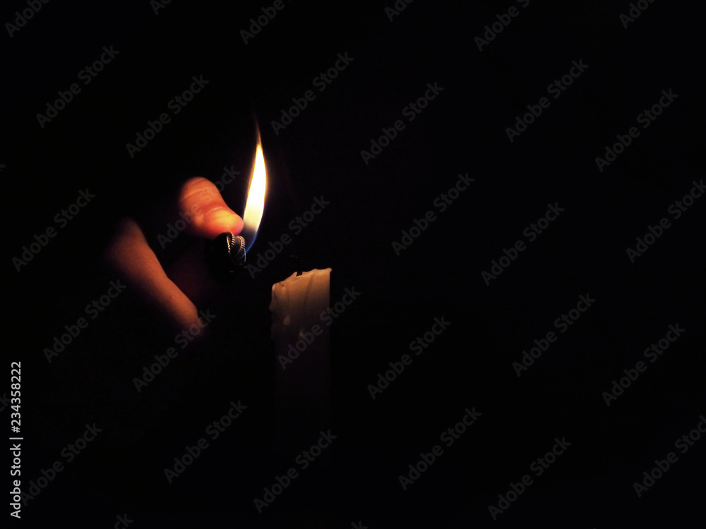 A person lights a candle with a lighter on darkness night. Close-up A person lights a candle with a lighter on darkness night. Close-up