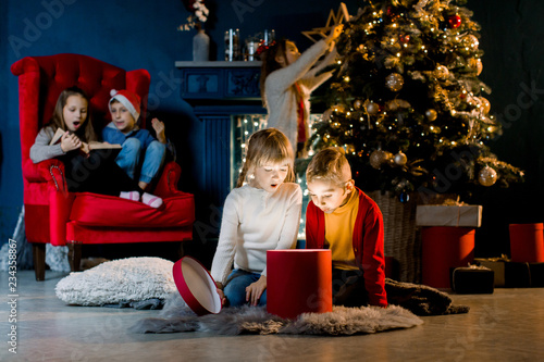 Cozy room decorated in a Christmas style. Beautiful children view a magical gift and prepare for the holiday