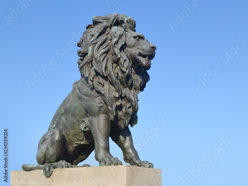 Old statue of a lion on a stone pedestal against the blue sky close up