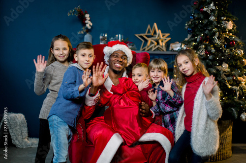 African Santa Claus and happy little children on the background of the Christmas tree