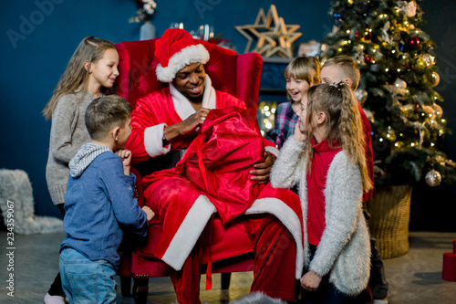 African Santa Claus takes gifts from a red bag for gifts and presents them to small, beautiful children.