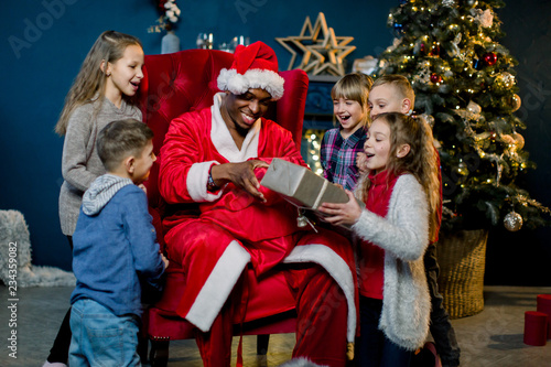 African Santa Claus takes gifts from a red bag for gifts and presents them to small, beautiful children.